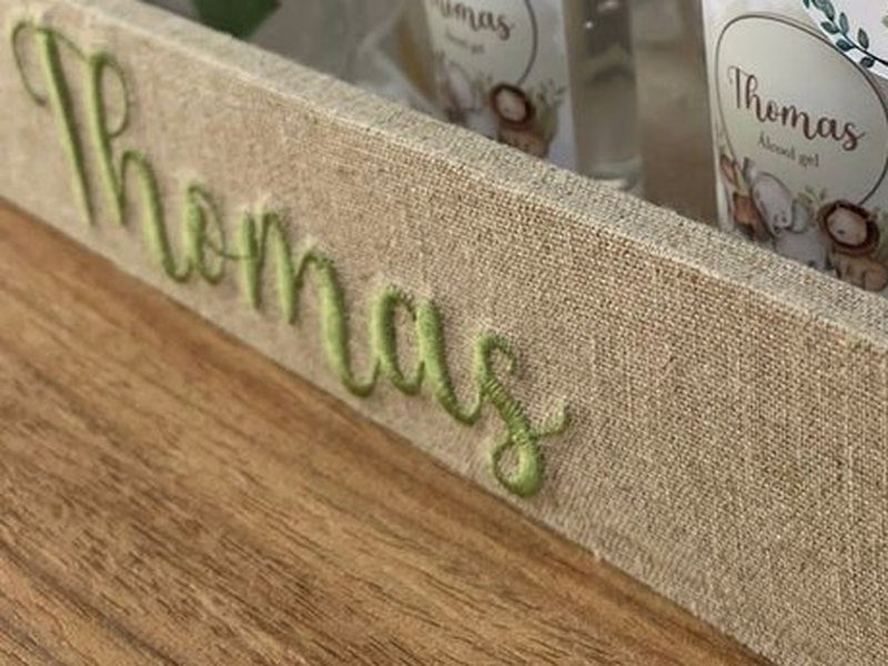 Thomas bordado em verde em cursiva no linho da lateral da bandeja, com o bordado em relevo destacado do tecido