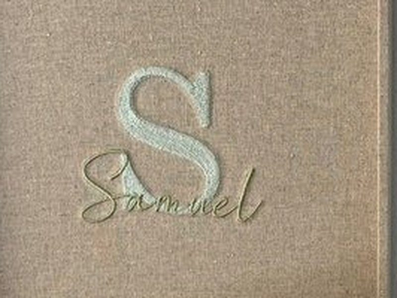 Inicial S bordada em relevo branco na face interna da tampa, com o nome Samuel bordado em verde atravessando por cima