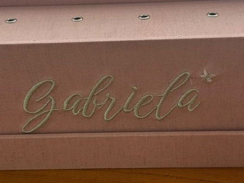 O nome Gabriela bordado por inteiro em fio verde-claro na lateral frontal da caixa, com uma borboleta bordada ao lado