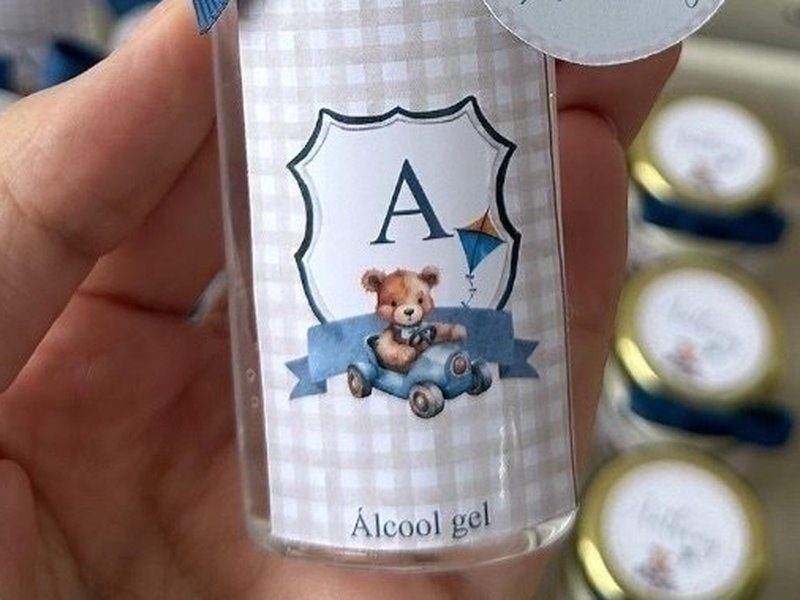 R�tulo xadrez bege com bras�o, a inicial A, um ursinho num carrinho azul e uma pipa; abaixo, a palavra �lcool gel