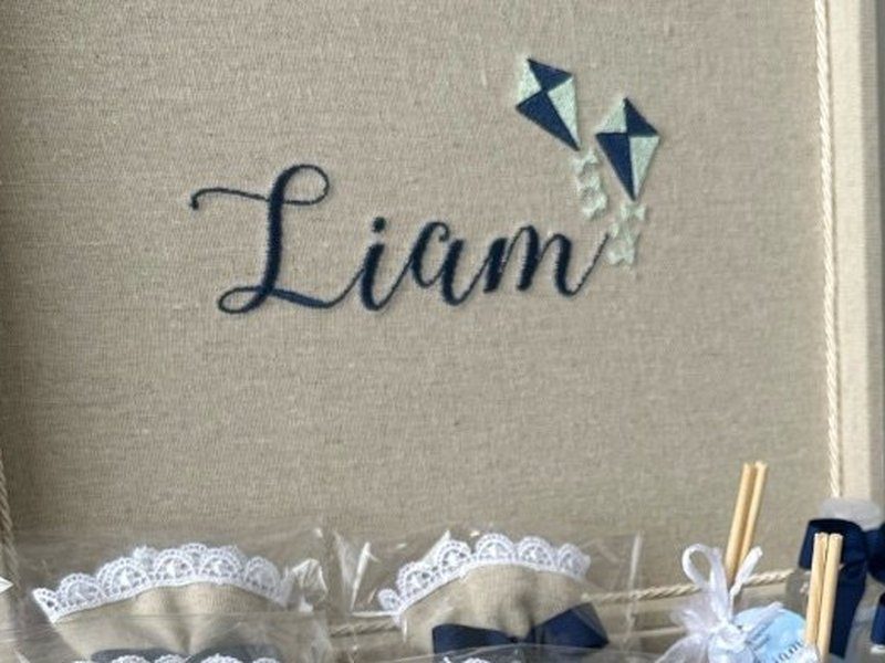 Liam bordado em azul escuro na tampa da caixa, com duas pipas bordadas ao lado e as linhas soltas