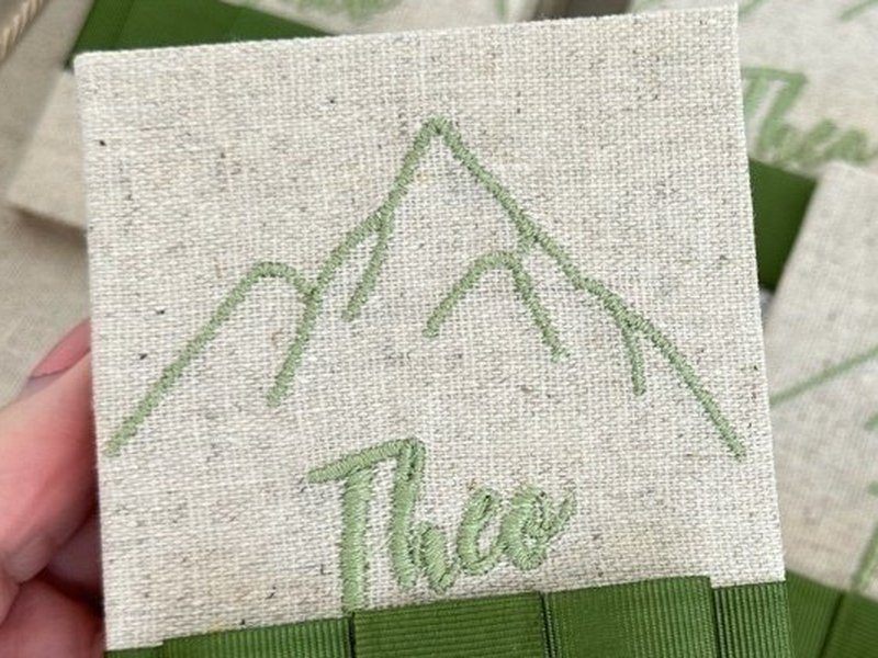 Outra capa do mesmo livrinho: montanhas bordadas em verde com Theo em cursiva abaixo