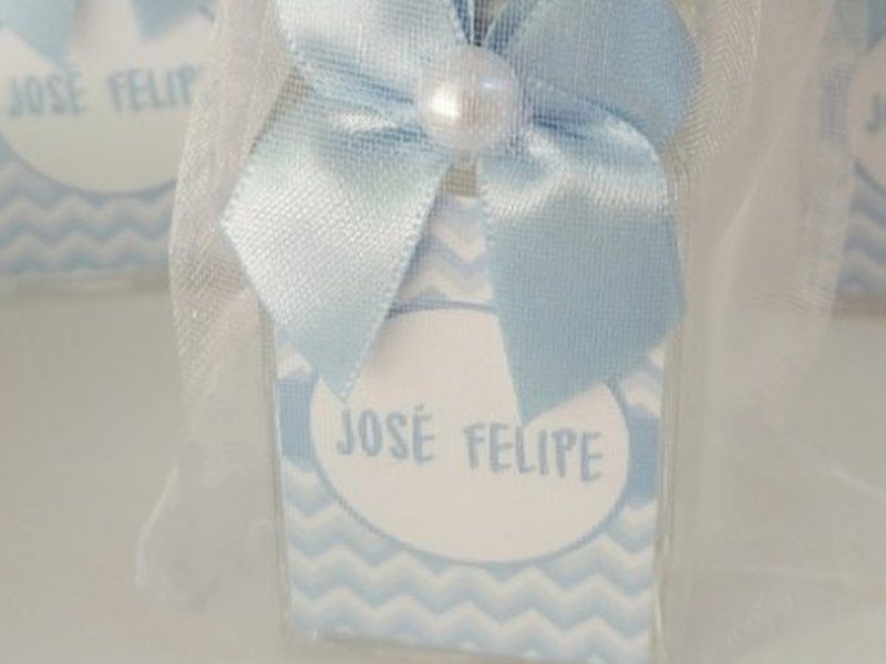 R�tulo chevron azul-claro com o nome JOS� FELIPE em caixa alta dentro de c�rculo branco, e la�o de cetim azul com meia-p�rola