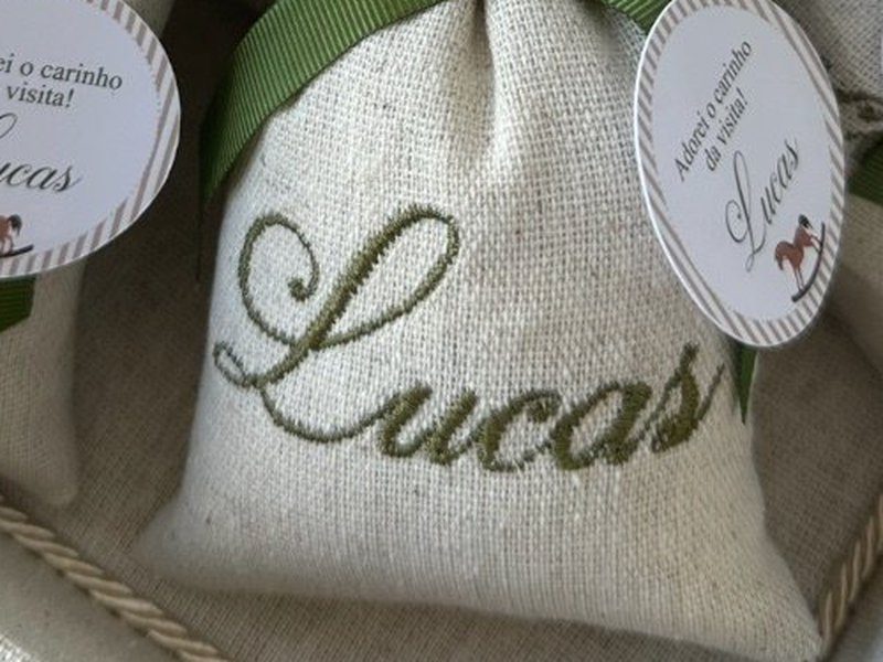 O nome Lucas bordado por inteiro em verde escuro em letra cursiva ligada, no linho cru do sach�