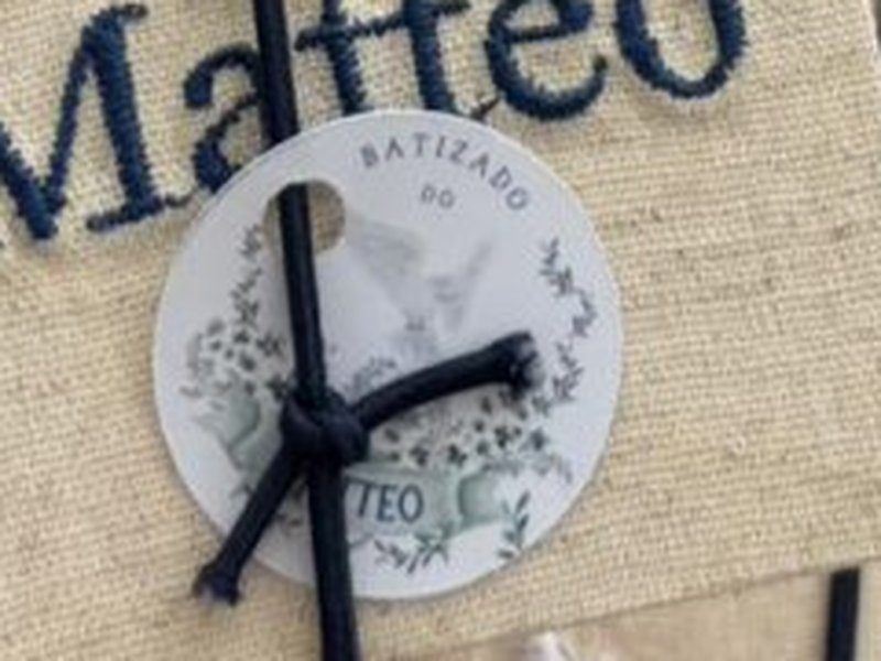 O el�stico azul escuro que fecha o livro no sentido vertical, prendendo a tag redonda com Batizado do Matteo