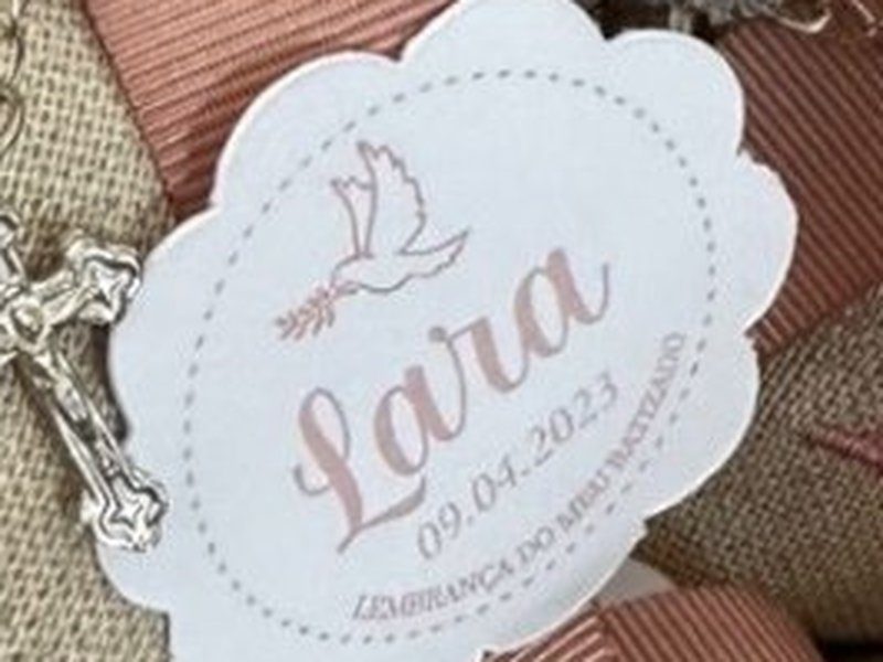 A tag recortada com pomba, o nome Lara e a data do batizado impressa