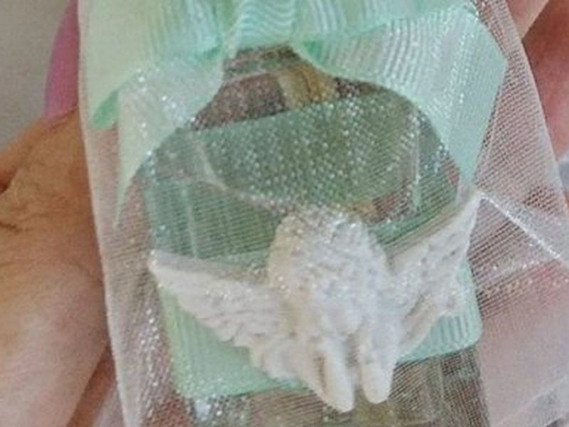 O anjo branco em relevo aplicado na frente do frasco de vidro, com as asas abertas, e o la�o verde no gargalo