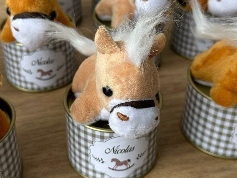O cavalinho de pel�cia inteiro: potro bege deitado, crina e cauda brancas, focinho branco e cabresto marrom, encaixado na boca da lata aberta