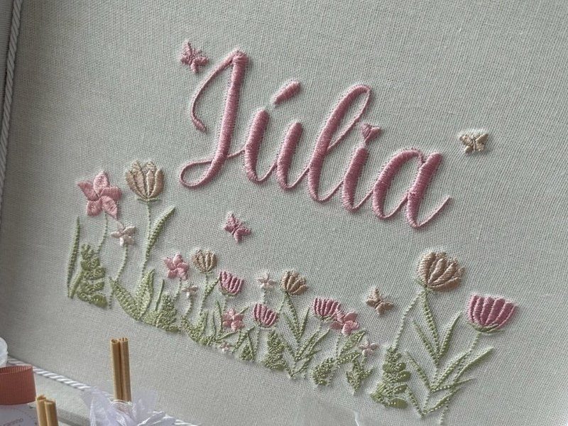 O nome J�lia em cursiva rosa sobre uma fileira de tulipas e folhagem bordadas, com borboletas soltas ao redor