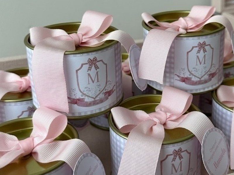 A lata de tampa dourada com r�tulo de bras�o trazendo a inicial M e um la�o desenhado, amarrada com fita rosa