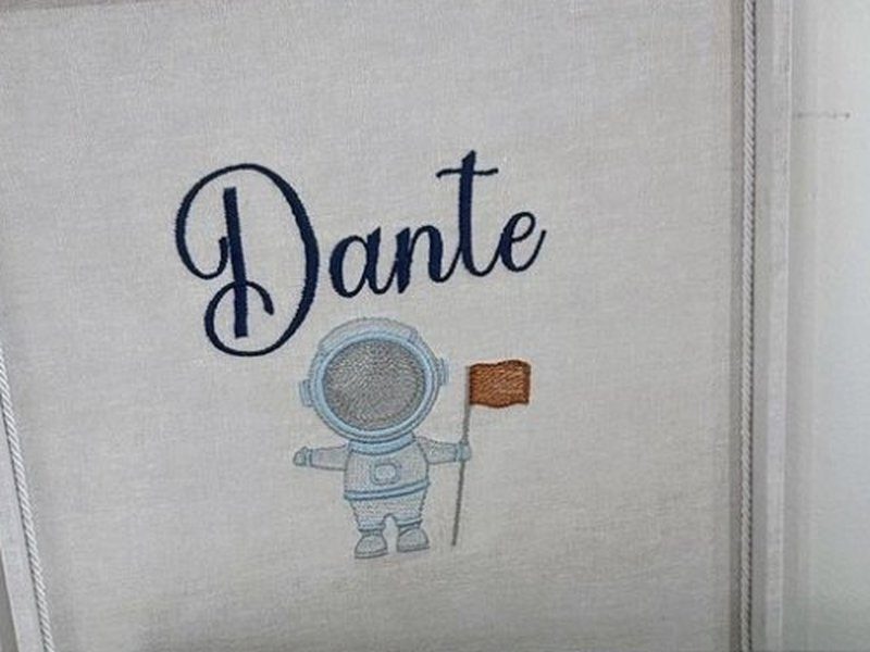 Dentro da tampa, o nome Dante em cursiva azul escuro e um astronauta bordado segurando uma bandeira