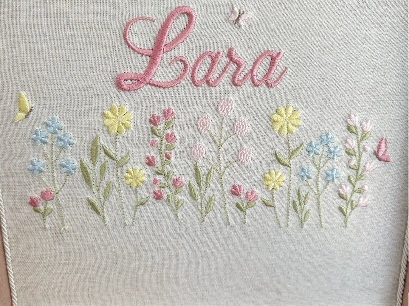 A faixa de jardim bordada por inteiro: flores azuis, amarelas e rosas com hastes verdes e borboletas nas duas pontas
