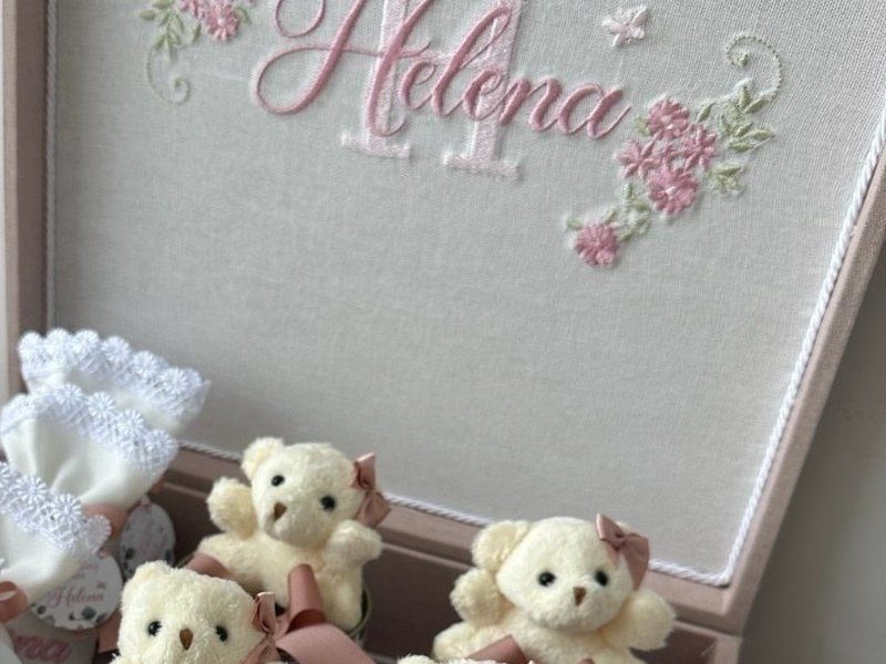 O nome Helena em cursiva rosa sobre um H mai�sculo, ladeado por ramos de flores rosas bordados dentro da tampa