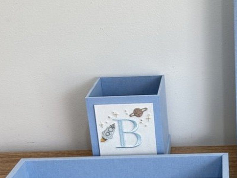 Cachep� c�bico aberto, em azul liso, com painel de linho branco trazendo o B bordado, um foguete e um planeta