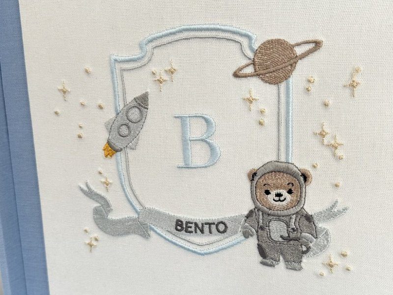 Bras�o bordado por inteiro: escudo azul-claro, foguete com chama, Saturno, estrelas em relevo, o B azul e o urso astronauta sobre a faixa BENTO