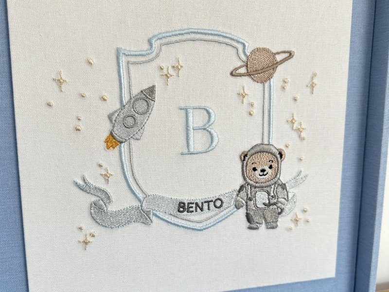 Painel de linho branco dentro da tampa com o bras�o bordado: foguete, Saturno, estrelas em relevo, B azul e urso astronauta sobre a faixa BENTO