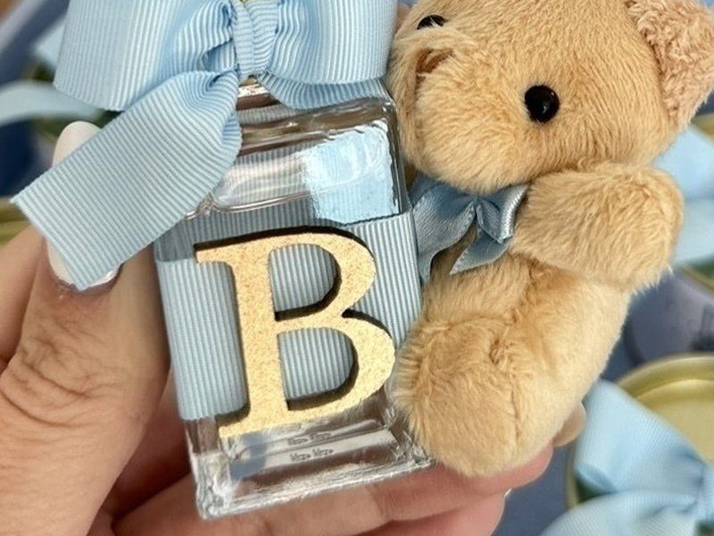 Frasco de vidro com faixa de gorgur�o azul listrado, a inicial B dourada inteira e o urso de pel�cia bege com la�o azul amarrado ao lado
