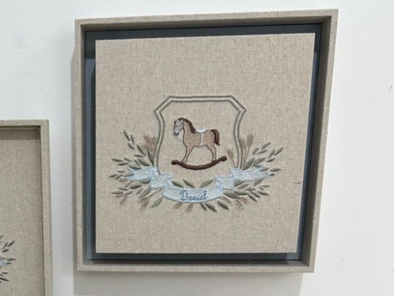 Quadro emoldurado com o bras�o bordado: cavalo de balan�o dentro do escudo, ramos e espigas, e faixa azul com Daniel