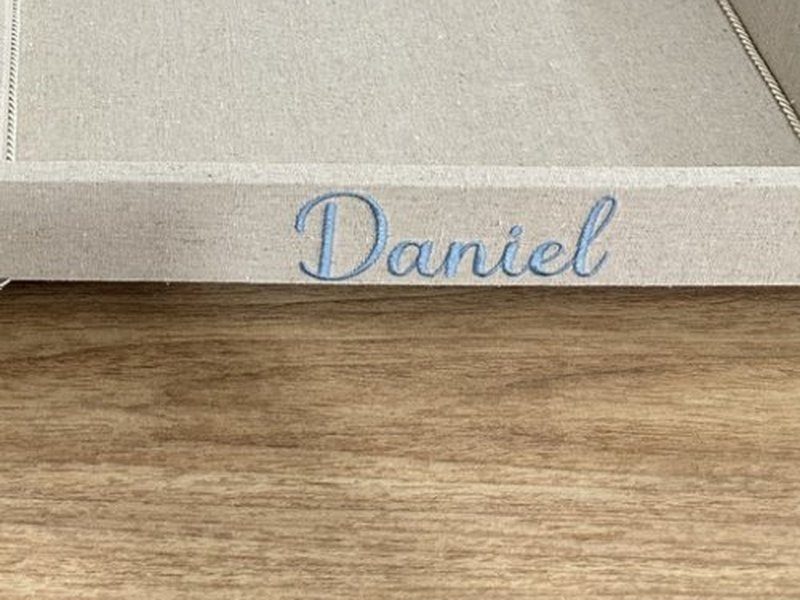 O nome Daniel bordado por inteiro em cursiva azul na lateral da bandeja, sobre os p�s de metal