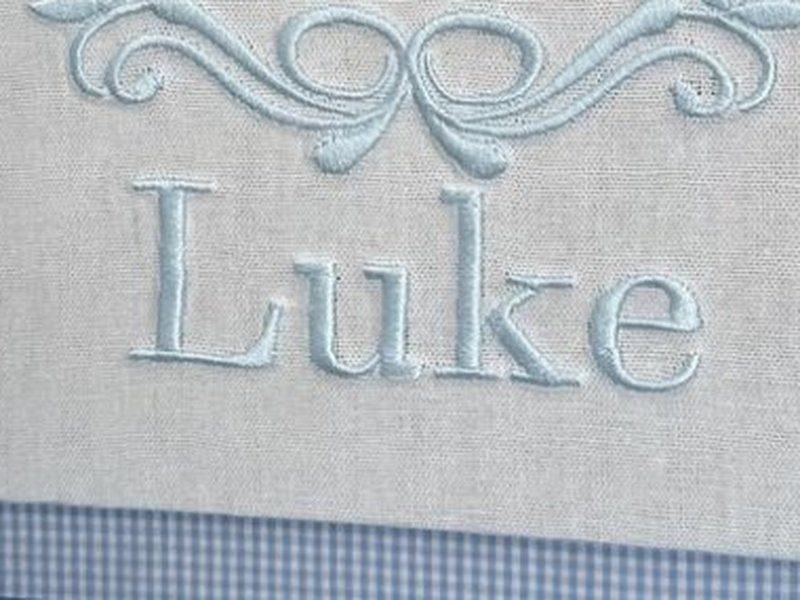 O nome Luke bordado por inteiro em letra serifada azul-clara, abaixo do la�o decorativo