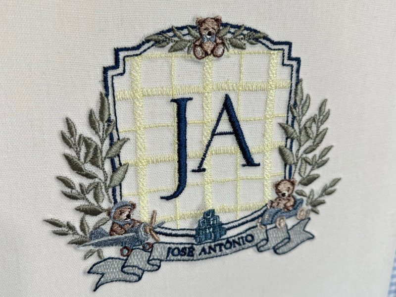 Escudo de grade amarela com JA, ramos de oliveira, ursinho no topo e dois pilotando um avi�o, faixa com JOS� ANT�NIO por extenso