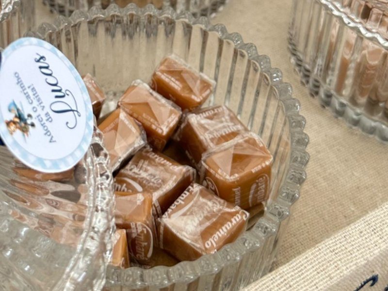 Baleiro de vidro canelado aberto, cheio de balas de caramelo embaladas