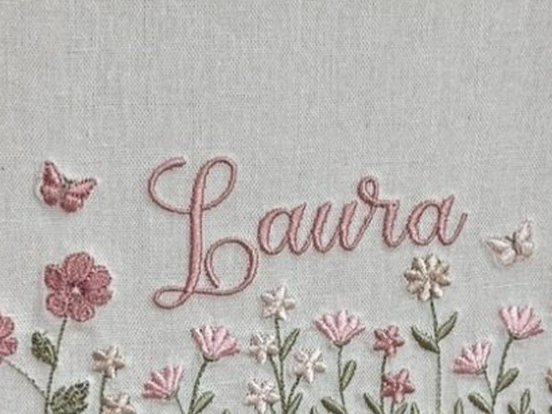 O nome Laura bordado por inteiro em cursiva rosa, com uma borboleta � esquerda e outra � direita
