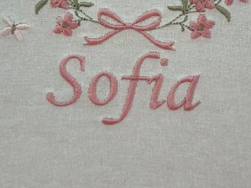 O nome Sofia bordado em cursiva rosa abaixo da coroa de flores