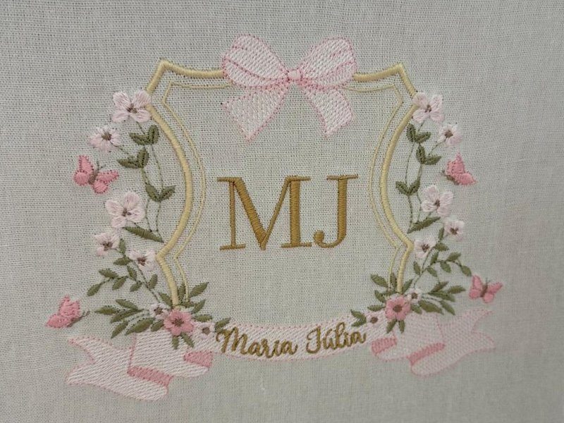 Bras�o bordado inteiro: MJ em ponto cheio dourado, moldura floral rosa, la�o xadrez, borboletas e faixa com Maria J�lia