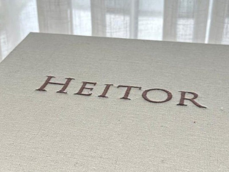 Nome HEITOR bordado em letras serifadas bord� sobre a tampa externa de linho