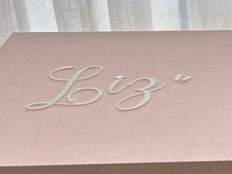 Nome Liz bordado em creme com borboleta na tampa externa da caixa fechada