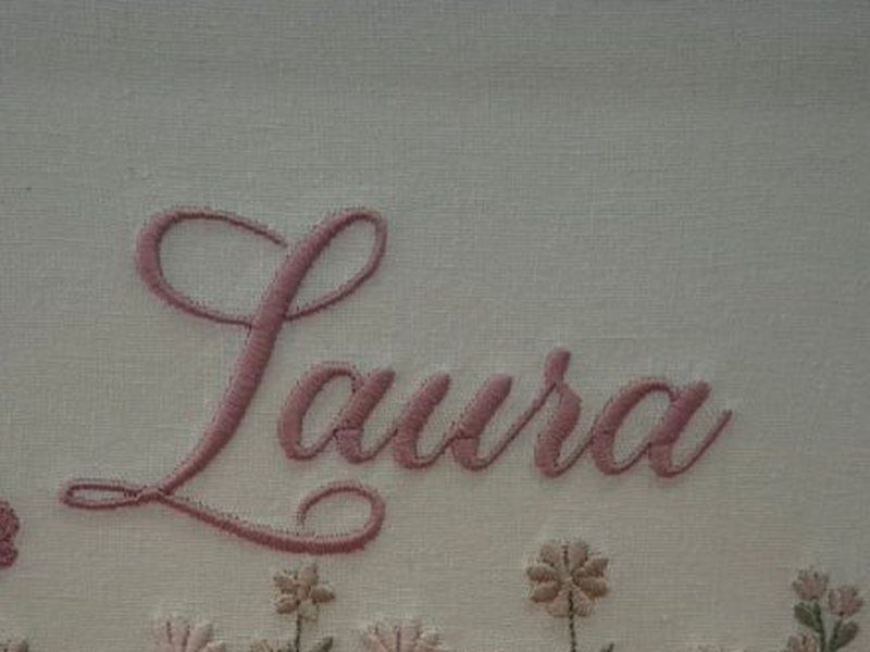 O nome Laura em cursiva rosa com o cord�o do ponto em relevo sobre o linho, dentro da caixa acr�lica