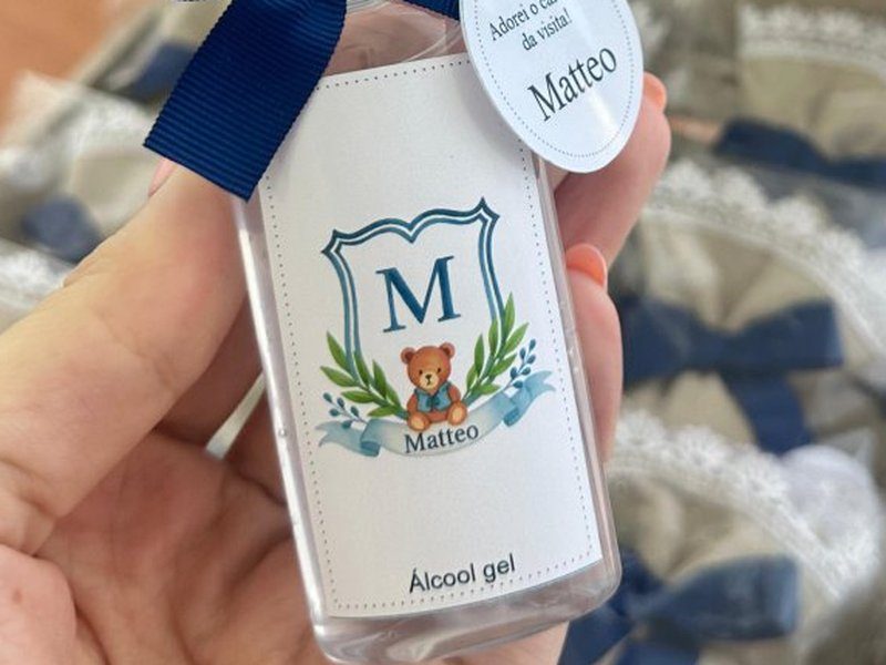 R�tulo impresso do frasco de �lcool gel repetindo o mesmo bras�o que aparece bordado na tampa ao fundo