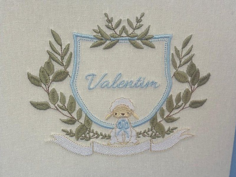 Escudo azul-claro com o nome Valentim, coroa de ramos de oliveira e ovelhinha de touca com la�o azul, sobre faixa branca