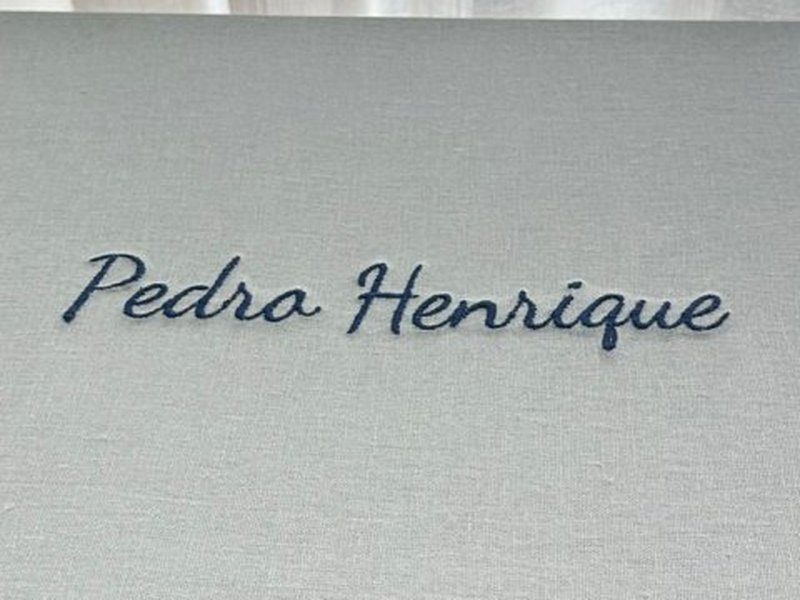 Pedro Henrique bordado por inteiro em cursiva azul escuro sobre o linho cinza-claro da tampa