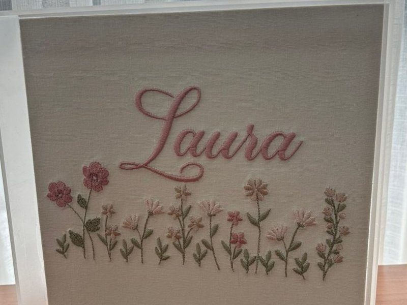 Quadro em caixa de acr�lico transparente com o bordado do nome Laura e canteiro de flores rosa em linho