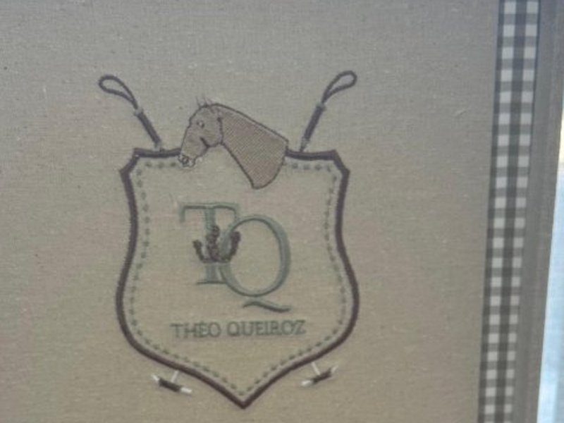 Cabe�a de cavalo de perfil com toca de j�quei, dois chicotes cruzados, monograma TQ e THEO QUEIROZ