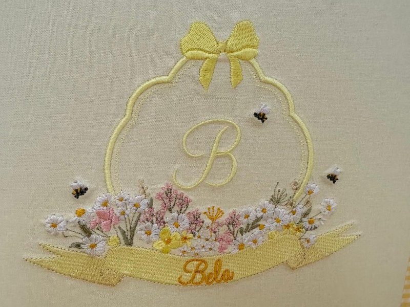 Moldura amarela com la�o, letra B em cursiva, canteiro de margaridas brancas e flores rosa, tr�s abelhas e faixa com Belo