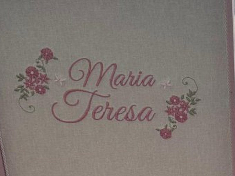 Maria Teresa bordado em duas linhas de cursiva rosa entre buqu�s de rosas e pequenas borboletas