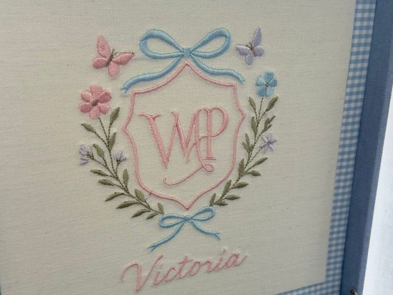 Escudo rosa com o monograma VP entrela�ado, la�o azul no topo e outro na base, ramos verdes, flores e duas borboletas, com Victoria em cursiva abaixo