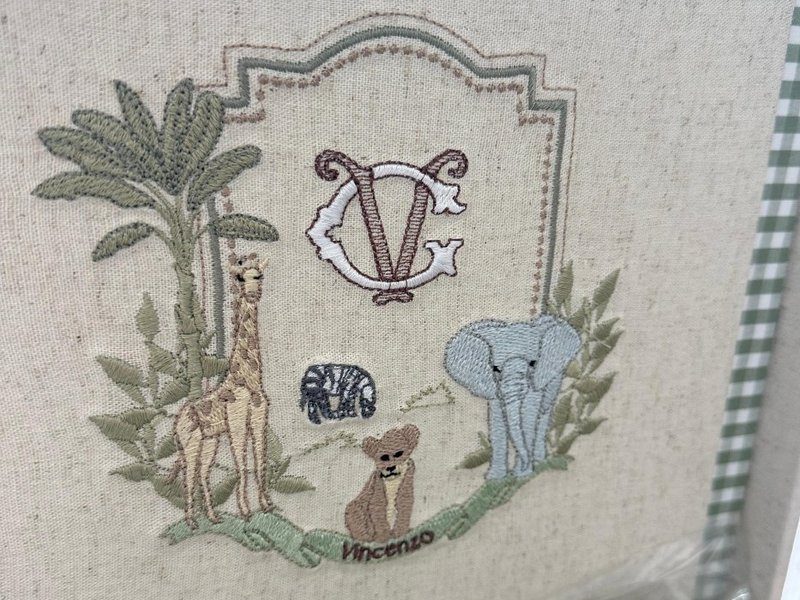 Escudo com monograma V branco contornado de marrom, girafa e palmeira � esquerda, zebra ao centro, le�ozinho sentado sobre a faixa Vincenzo e elefante � direita