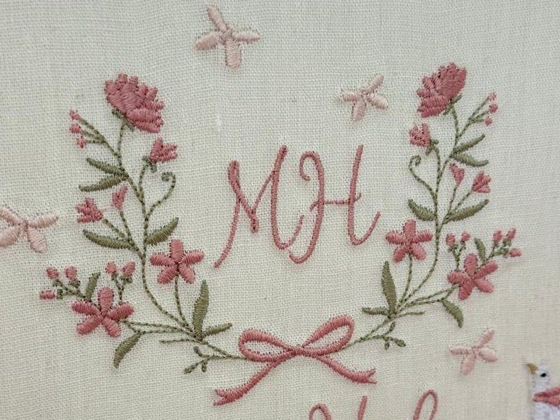 Coroa de flores rosa e folhas verdes em torno do monograma MH, com la�o rosa na base e lib�lulas em volta