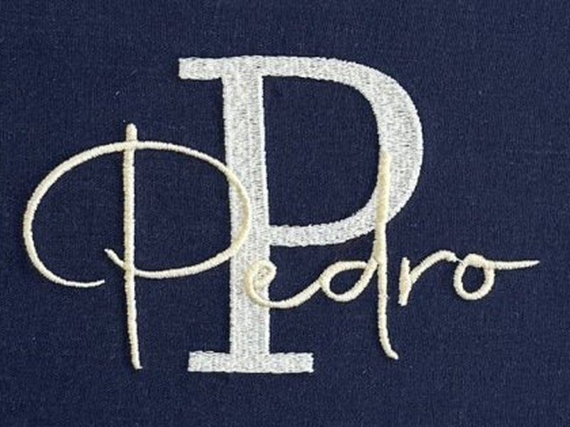 Letra P grande em bege prateado com o nome Pedro em cursiva creme escrito por cima, cruzando a haste do P