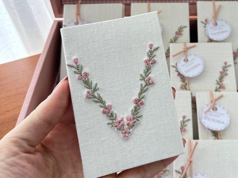 Capa do livrinho em linho cru com o ramo de flores rosa em V bordado, igual ao da tampa da caixa