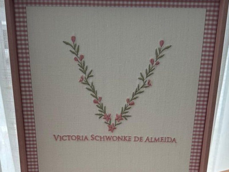 O nome completo Victoria Schwonke de Almeida bordado em mai�sculas rosa abaixo do ramo em V