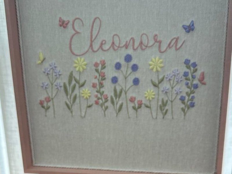 Canteiro bordado com flores lil�s, amarelas, azuis e rosa sob o nome