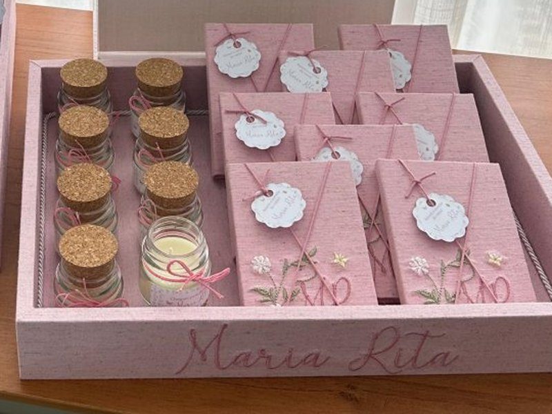 'Maria Rita' bordado em rosa na lateral frontal da bandeja, com as velas e os livrinhos acomodados dentro