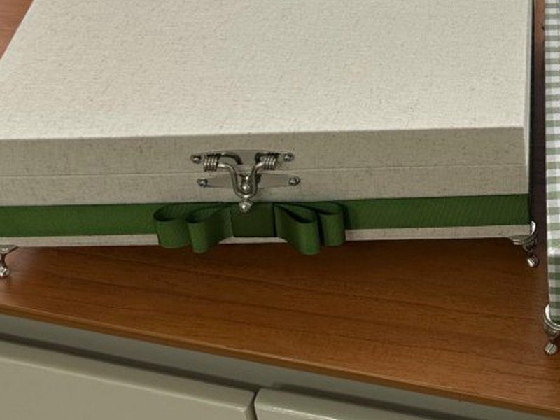 O fecho met�lico, a fita verde com la�o em volta da base e os p�s prateados da caixa