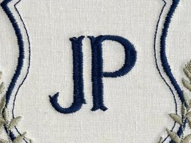 Monograma JP bordado em serifa azul escuro, dentro do escudo de contorno duplo