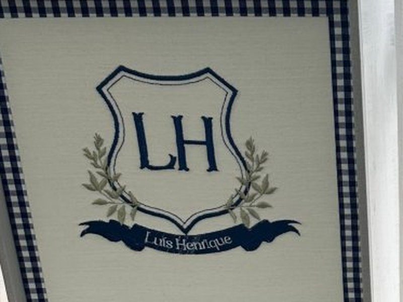 Escudo azul escuro com o monograma LH, ramos de louro verdes e faixa marinho com 'Lu�s Henrique' em cursiva